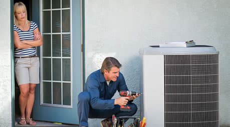 An HVAC technician servicing an outdoor condenser unit